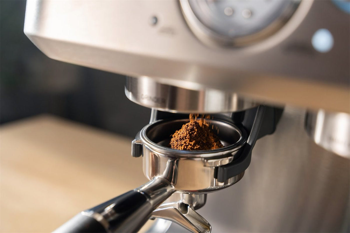 Malet kaffe drysser ned i et portafilter under kværnen på en espressomaskine i stål