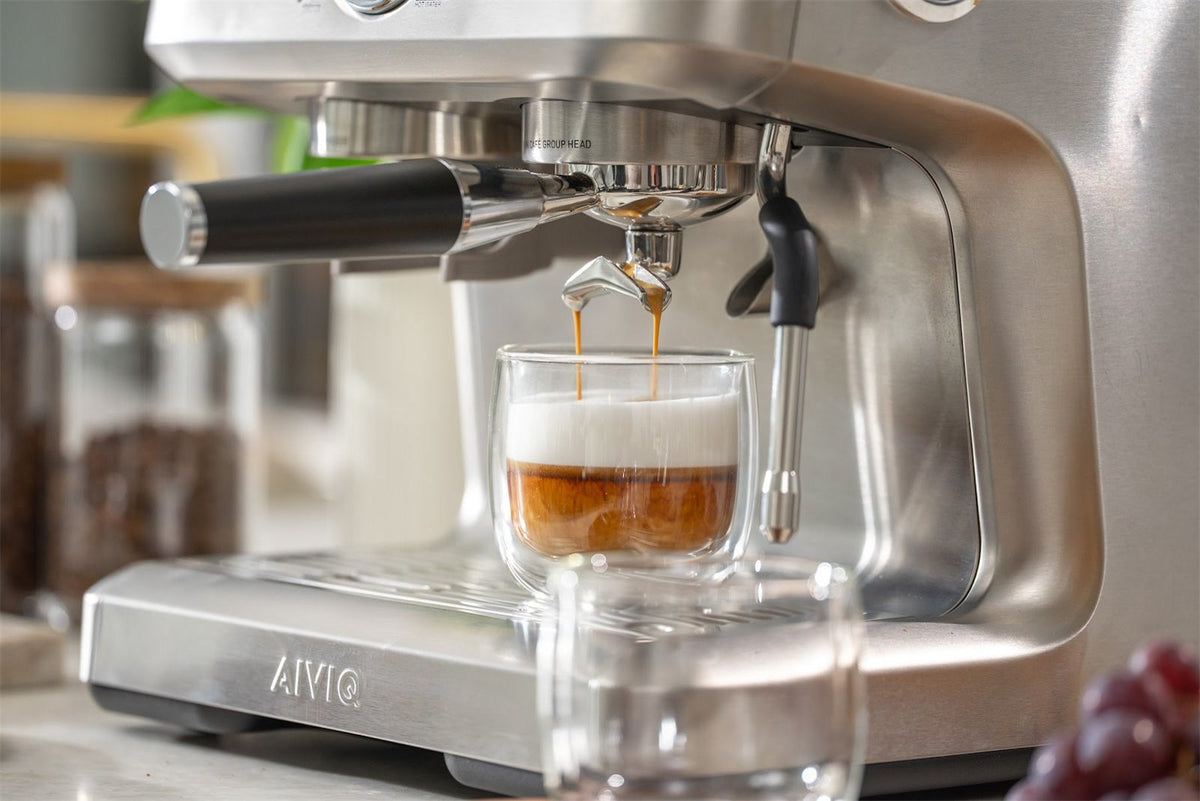 Espresso løber fra portafiltrets to tude ned i et glas med varm mælk på en espressomaskine i stål