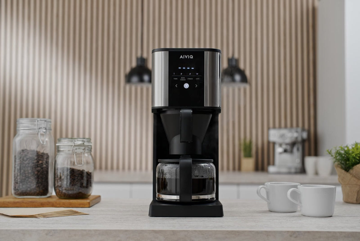 AIVIQ Grind 'N Brew Inspire med fuld glaskande på et køkkenbord, to glas med kaffebønner og to hvide kopper