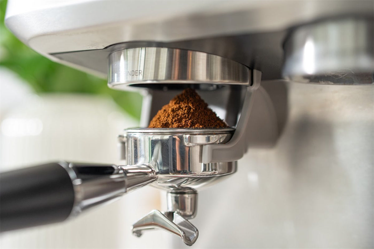 Nymalet kaffe ligger i en top i portafiltret, der sidder i holderen under kværnen på en espressomaskine i stål