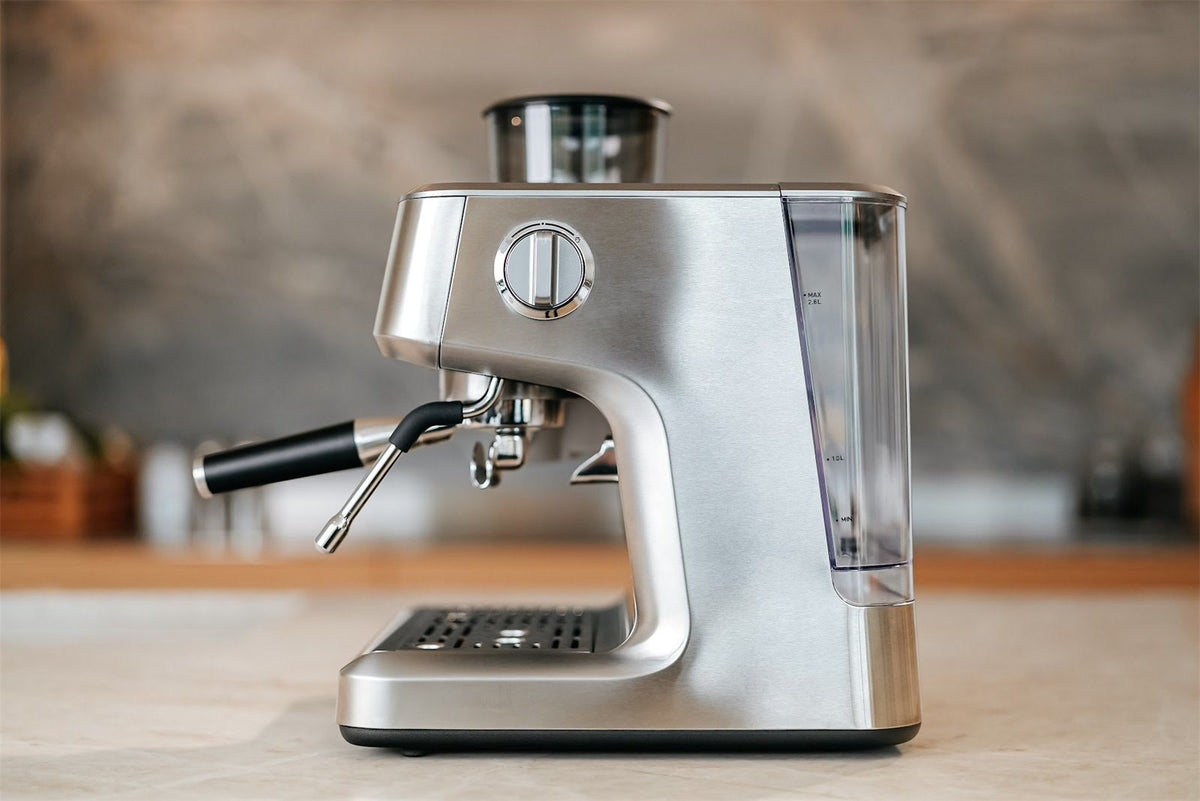 Espressomaskine i stål set fra siden med dampstav, portafilter og vandtank på et lyst køkkenbord