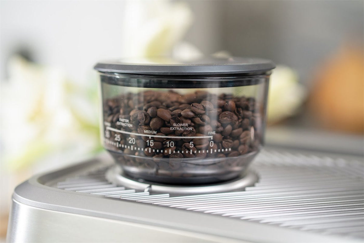 Bønnebeholder med kaffebønner og en skala fra fin til grov oven på en espressomaskine i stål