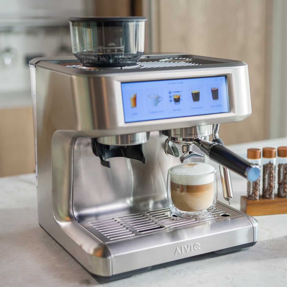Aspire Expert set skråt fra venstre med et dobbeltvægget glas med kaffe og et tykt lag mælkeskum på drypbakken. Skærmen står i Simple mode.