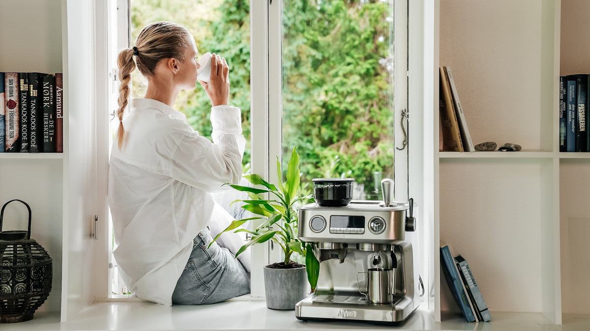 En kvinde drikker morgenkaffe ved vinduet med Aspire Advanced i baggrunden