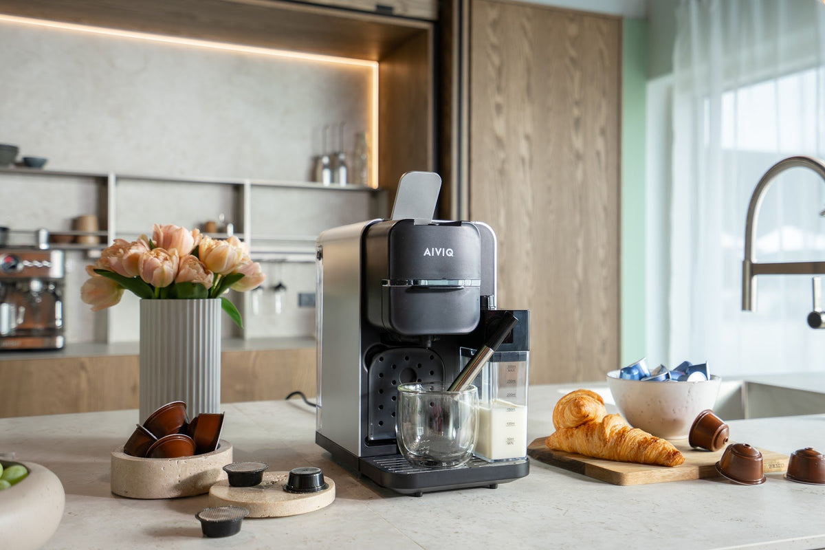 AIVIQ MultiBrew Pro på et køkkenbord med forskellige kapsler, tulipaner og croissanter